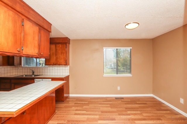 kitchen featuring sink, tasteful backsplash, tile counters, light hardwood / wood-style floors, and kitchen peninsula