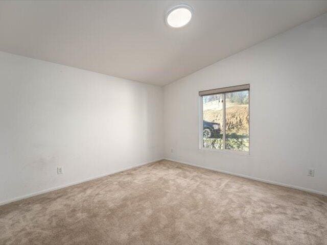 spare room featuring light colored carpet and lofted ceiling