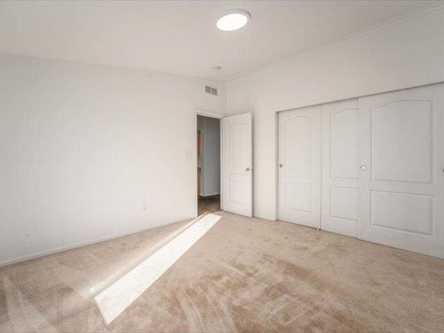 unfurnished bedroom with light colored carpet and a closet