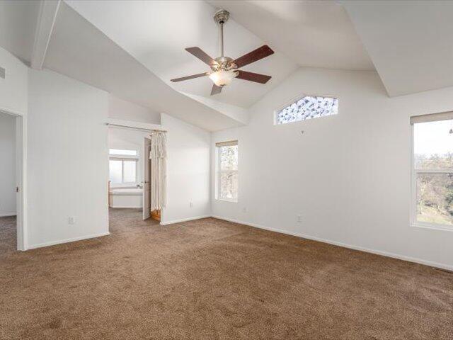 carpeted spare room with ceiling fan and vaulted ceiling