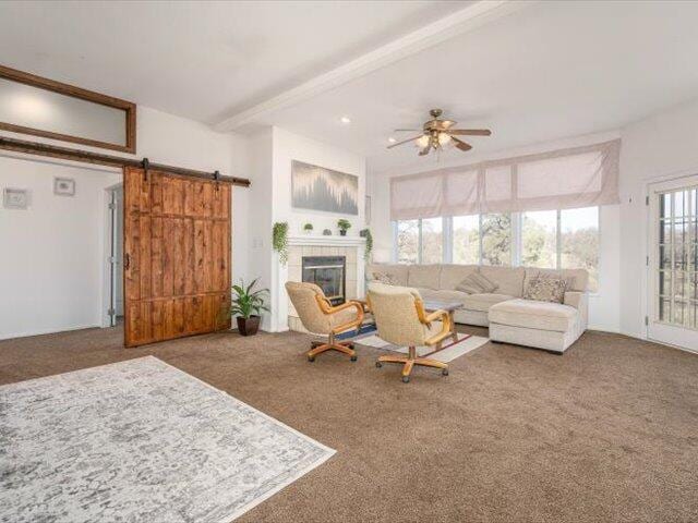 living room with ceiling fan, a tile fireplace, beam ceiling, a barn door, and carpet floors