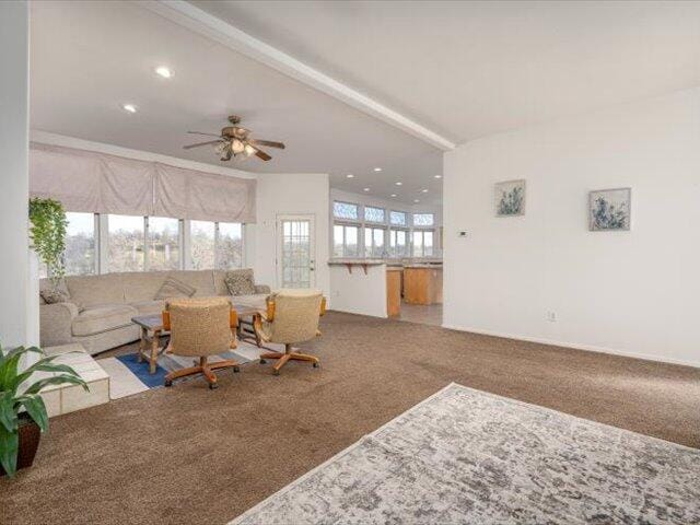 living room with ceiling fan, beamed ceiling, and carpet