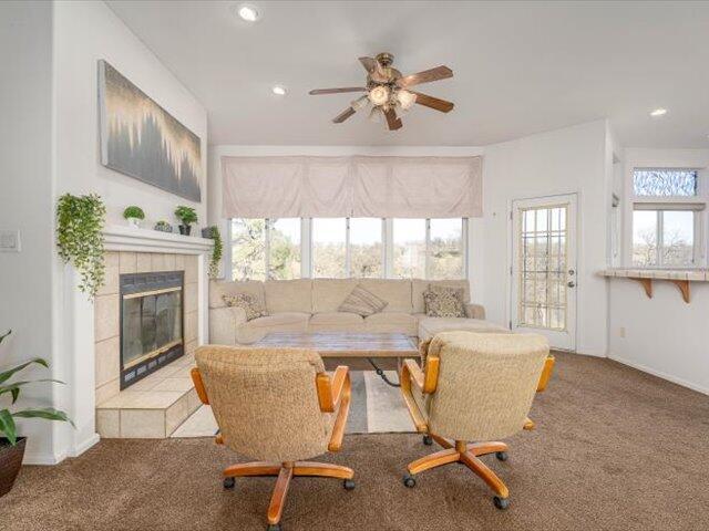 living room with carpet flooring, ceiling fan, and a tiled fireplace