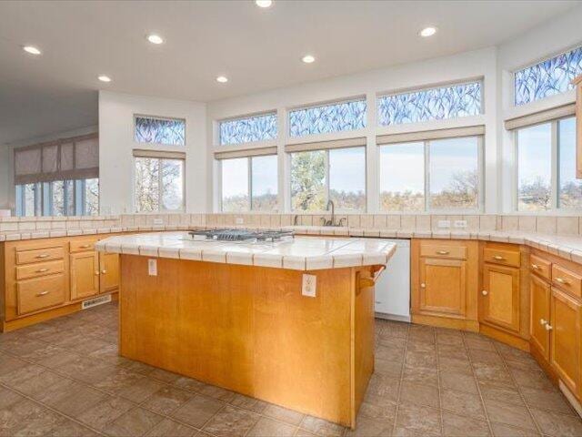 kitchen with sink, tile counters, stainless steel gas cooktop, white dishwasher, and a kitchen island