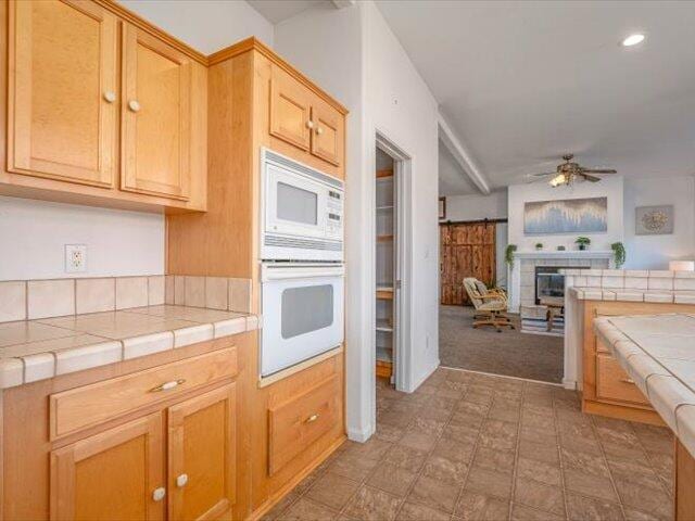 kitchen featuring tile counters, ceiling fan, white appliances, and light brown cabinetry