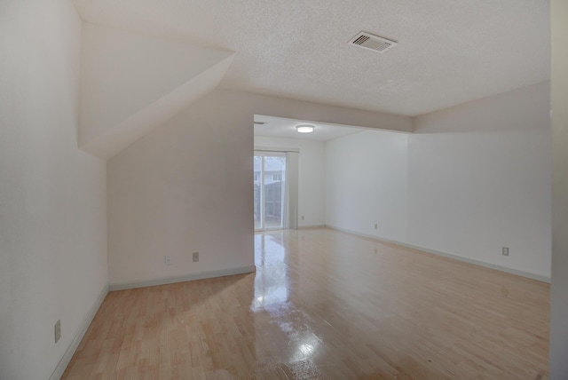 additional living space with lofted ceiling, light wood-type flooring, and a textured ceiling