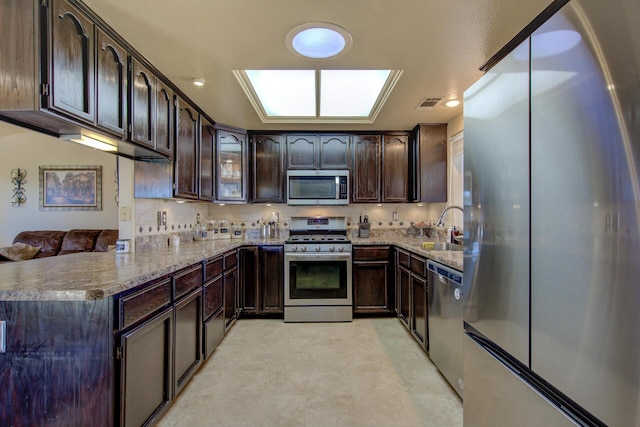 kitchen with appliances with stainless steel finishes, sink, backsplash, kitchen peninsula, and dark brown cabinets