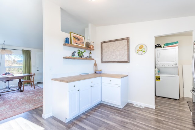 kitchen featuring wooden counters, white cabinets, vaulted ceiling, light wood-type flooring, and stacked washing maching and dryer