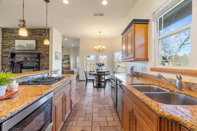 kitchen with light stone countertops, appliances with stainless steel finishes, sink, a chandelier, and hanging light fixtures