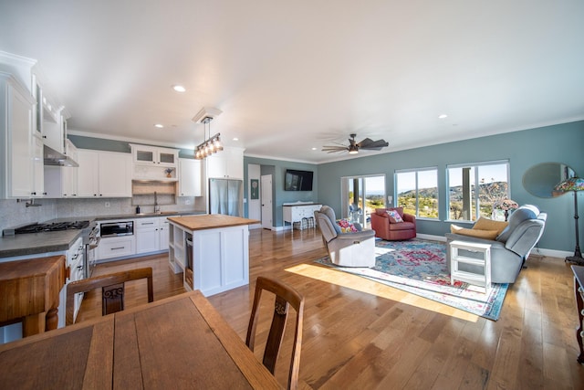 kitchen with a center island, wooden counters, white cabinetry, hanging light fixtures, and stainless steel fridge