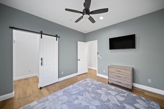 bedroom with ceiling fan, light hardwood / wood-style floors, and a barn door