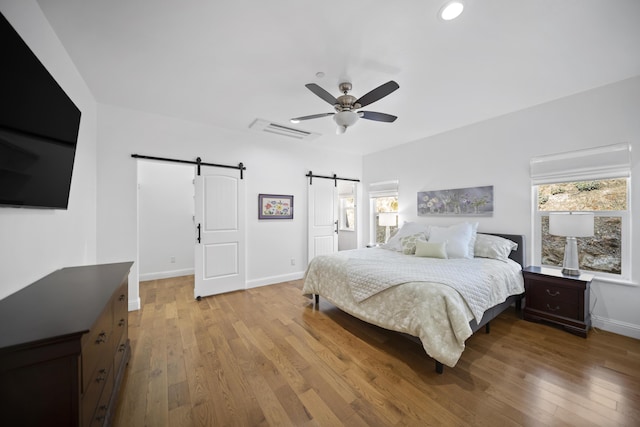 bedroom featuring ceiling fan, a barn door, and hardwood / wood-style flooring