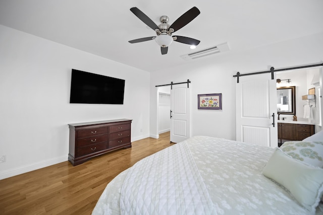 bedroom with ensuite bath, a barn door, ceiling fan, and light hardwood / wood-style flooring