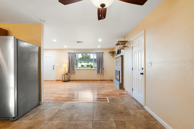 kitchen with stainless steel fridge, ceiling fan, and a brick fireplace