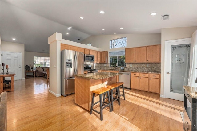 kitchen with appliances with stainless steel finishes, a kitchen bar, a kitchen island, light hardwood / wood-style flooring, and backsplash