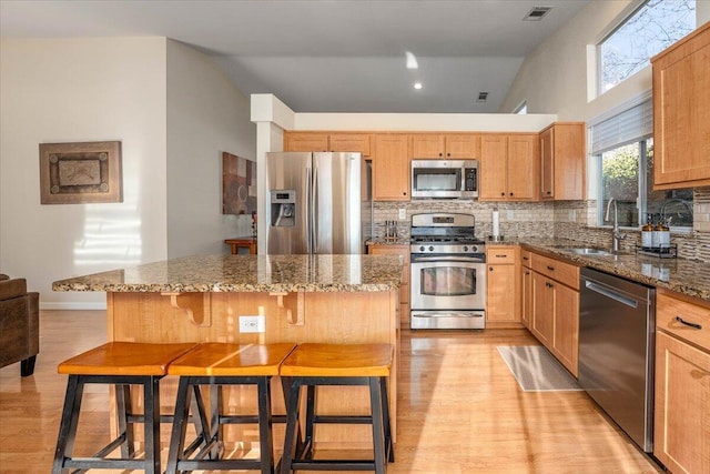 kitchen with appliances with stainless steel finishes, dark stone counters, a kitchen bar, a kitchen island, and sink