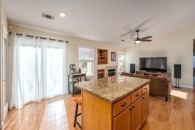 kitchen featuring light stone counters, light hardwood / wood-style flooring, a center island, a breakfast bar, and ceiling fan