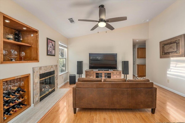 living room featuring light hardwood / wood-style floors, ceiling fan, a tile fireplace, and lofted ceiling