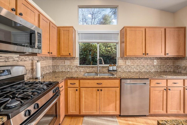 kitchen featuring vaulted ceiling, stainless steel appliances, decorative backsplash, stone countertops, and sink