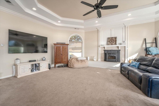 carpeted living room with ceiling fan, crown molding, a tray ceiling, and a wood stove