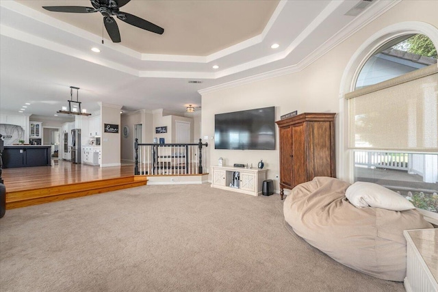 living room featuring ceiling fan with notable chandelier, carpet, a tray ceiling, and ornamental molding