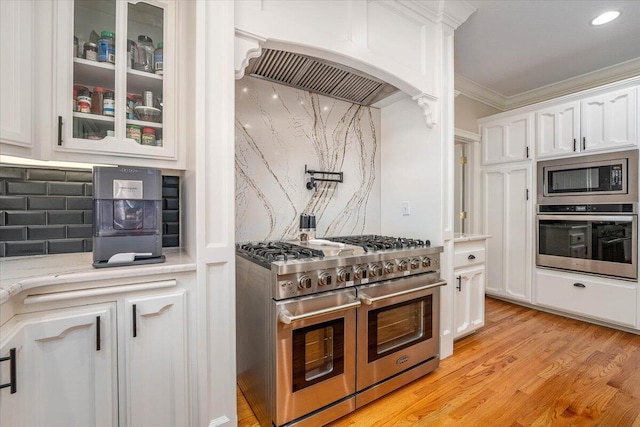 kitchen with decorative backsplash, light hardwood / wood-style flooring, appliances with stainless steel finishes, ornamental molding, and white cabinets