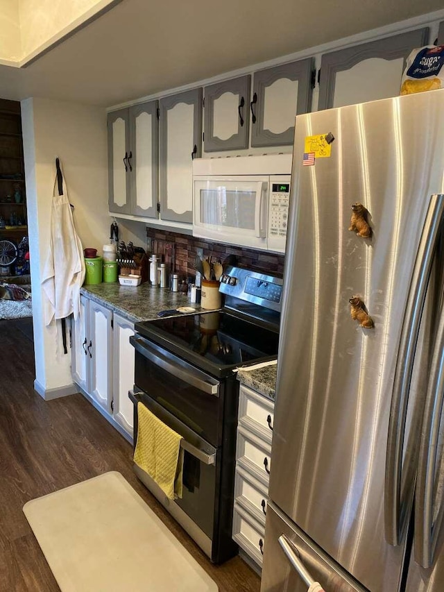 kitchen with dark wood-type flooring, appliances with stainless steel finishes, dark stone counters, and gray cabinetry