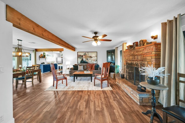 living room with beam ceiling, wood-type flooring, ceiling fan with notable chandelier, and a brick fireplace