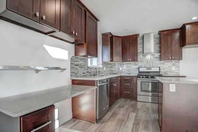 kitchen featuring wall chimney range hood, sink, light wood-type flooring, appliances with stainless steel finishes, and light stone counters