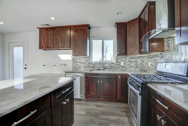 kitchen with light stone countertops, gas range, wall chimney range hood, sink, and dishwasher