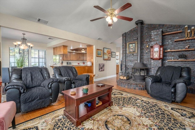 living room featuring a wood stove, brick wall, wood-type flooring, lofted ceiling, and ceiling fan with notable chandelier