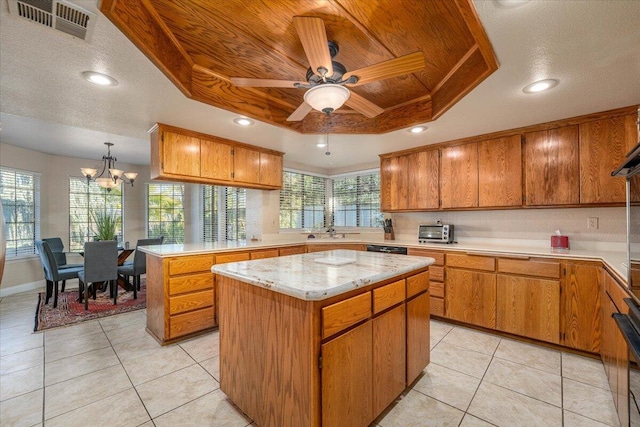 kitchen featuring a tray ceiling, a center island, light tile patterned flooring, and ceiling fan with notable chandelier