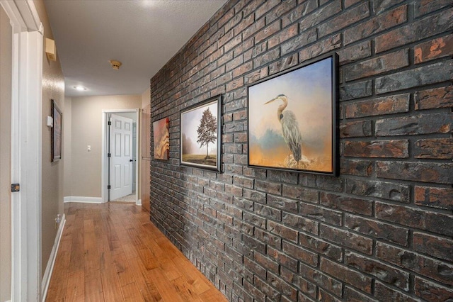 corridor with wood-type flooring and brick wall