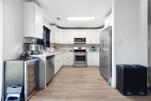 kitchen with beverage cooler, white cabinets, backsplash, stainless steel appliances, and light hardwood / wood-style flooring