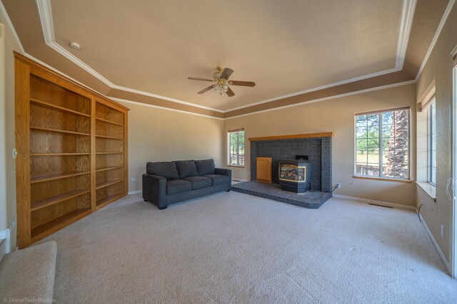 living room with carpet, ceiling fan, a wood stove, and crown molding