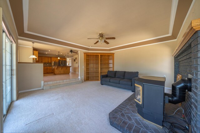 carpeted living room featuring a raised ceiling, a wood stove, ceiling fan, and crown molding