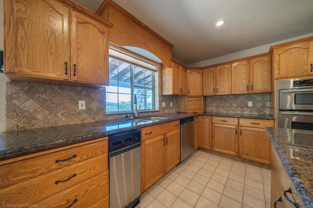 kitchen featuring sink, tasteful backsplash, dark stone counters, light tile patterned floors, and appliances with stainless steel finishes