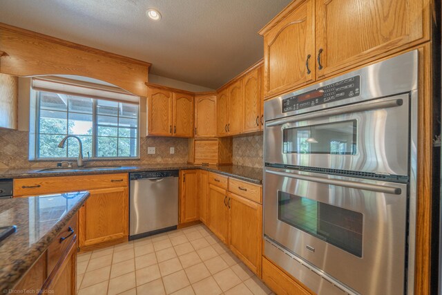 kitchen featuring decorative backsplash, appliances with stainless steel finishes, dark stone counters, sink, and light tile patterned flooring