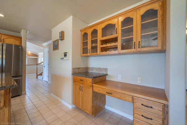 kitchen featuring stainless steel refrigerator, dark stone countertops, lofted ceiling, light tile patterned flooring, and built in desk