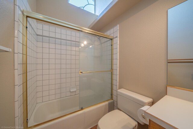 full bathroom featuring combined bath / shower with glass door, vanity, and toilet