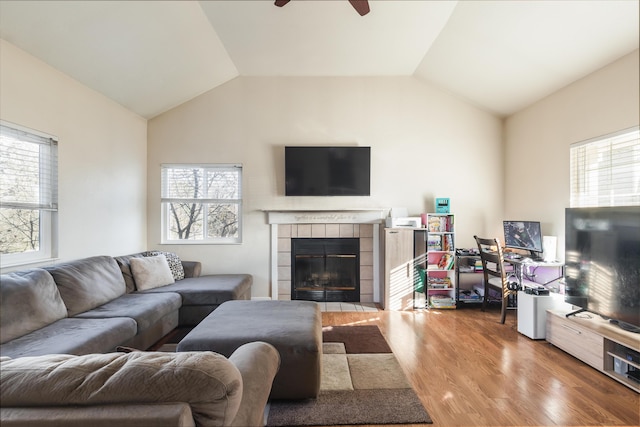 living room featuring a tiled fireplace, ceiling fan, wood-type flooring, and vaulted ceiling