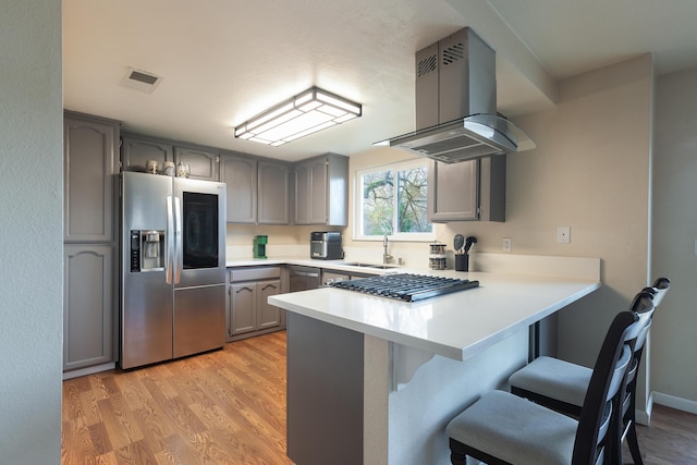 kitchen featuring kitchen peninsula, stainless steel refrigerator with ice dispenser, island range hood, sink, and gray cabinets