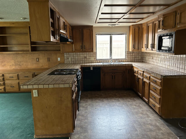 kitchen with sink, tile countertops, kitchen peninsula, decorative backsplash, and black appliances