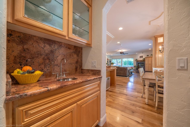 bar featuring ceiling fan, sink, backsplash, dark stone counters, and light wood-type flooring