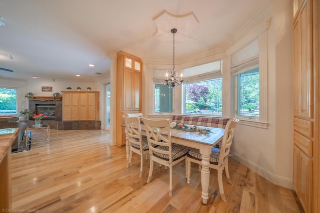 dining area featuring a tile fireplace, ornamental molding, a chandelier, and light wood-type flooring