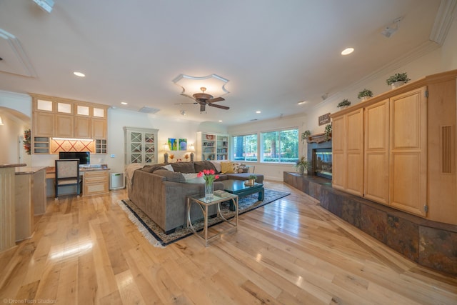 living room with ceiling fan, crown molding, built in desk, and light wood-type flooring