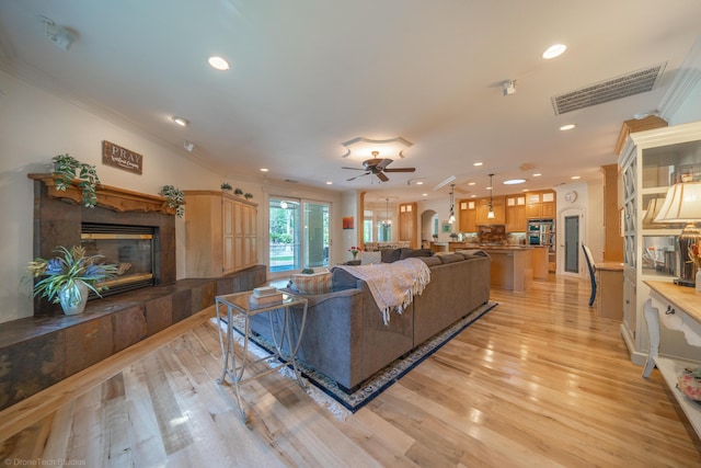 living room with ceiling fan, a fireplace, crown molding, and light wood-type flooring