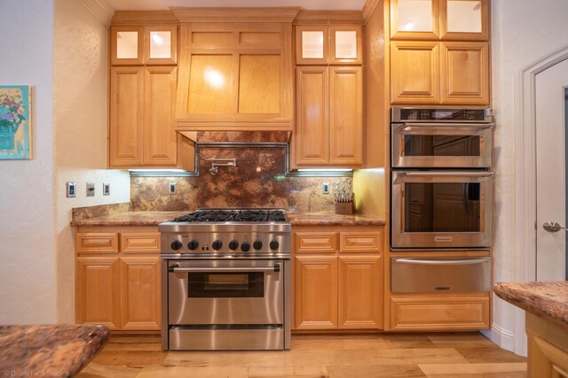 kitchen with backsplash, light wood-type flooring, light stone countertops, and stainless steel appliances