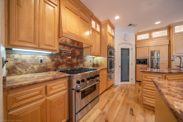 kitchen with backsplash, light stone counters, stainless steel appliances, sink, and light hardwood / wood-style floors