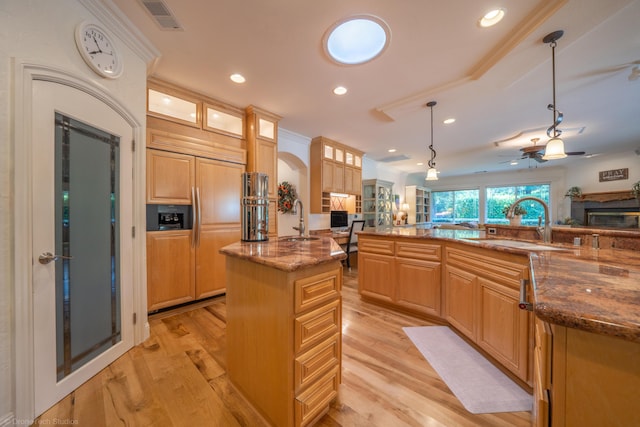 kitchen with paneled built in fridge, sink, ceiling fan, decorative light fixtures, and a kitchen island